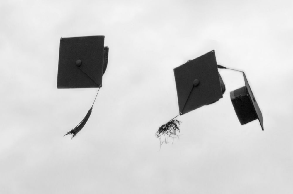 Graduation hats thrown up in the air against a grey cloudy day