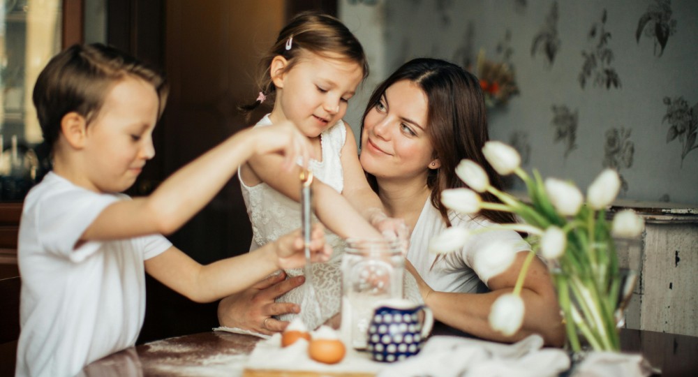 Mum with two young daughters baking at the kitchen table