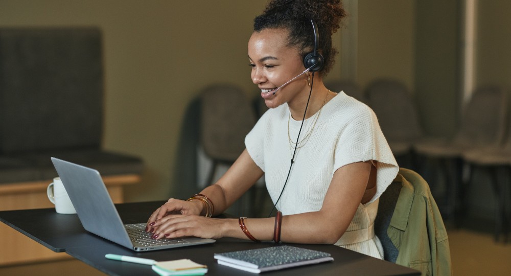 Happy young female working from home for an insurance company with headset and laptop 