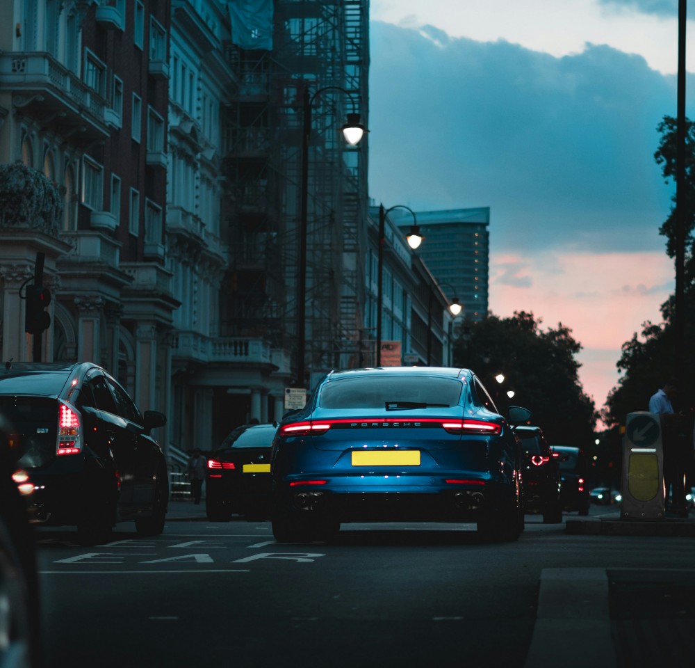 Blue porsche driving down a busy city road at rush hour