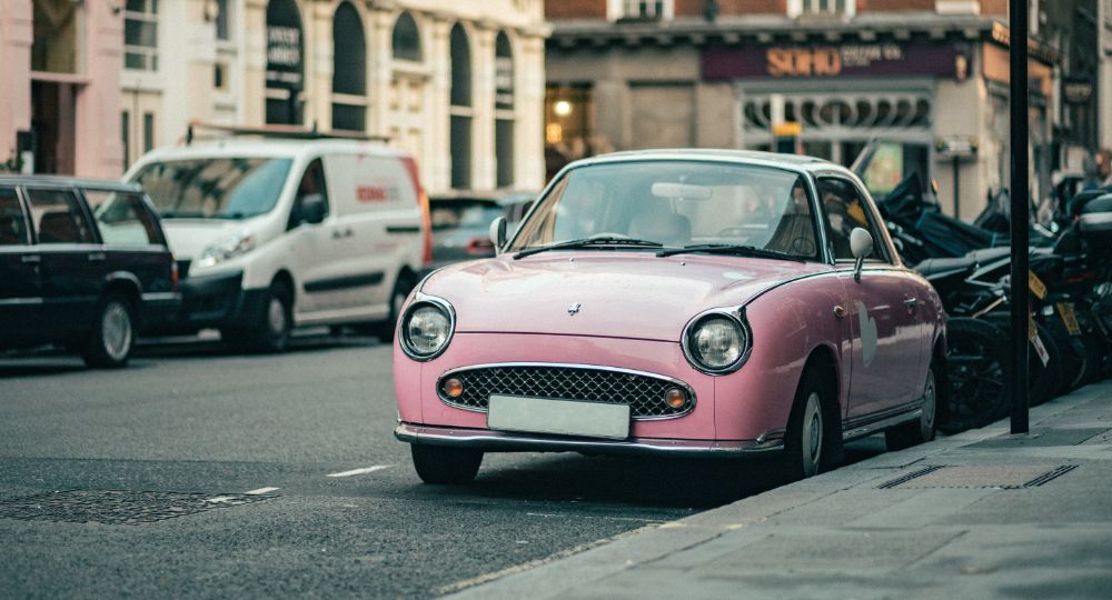 Baby pink Nissan Figaro parked at the side of the road in a city or town