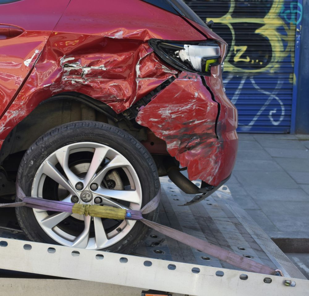 dented red car loaded onto a flatbed truck