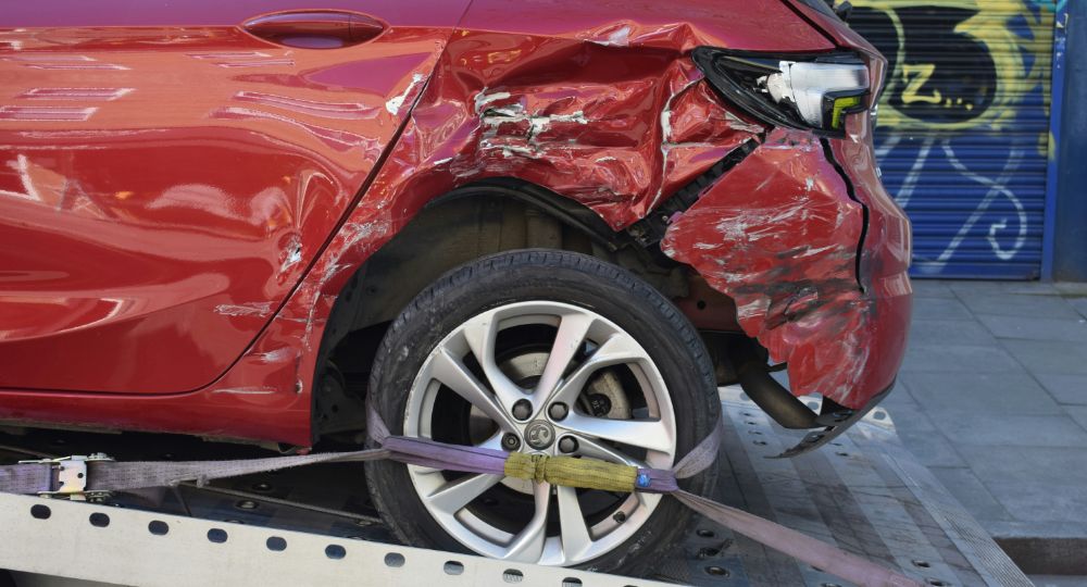 dented red car loaded onto a flatbed truck