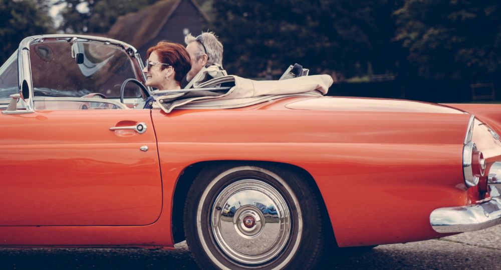 Older couple driving a red classic car