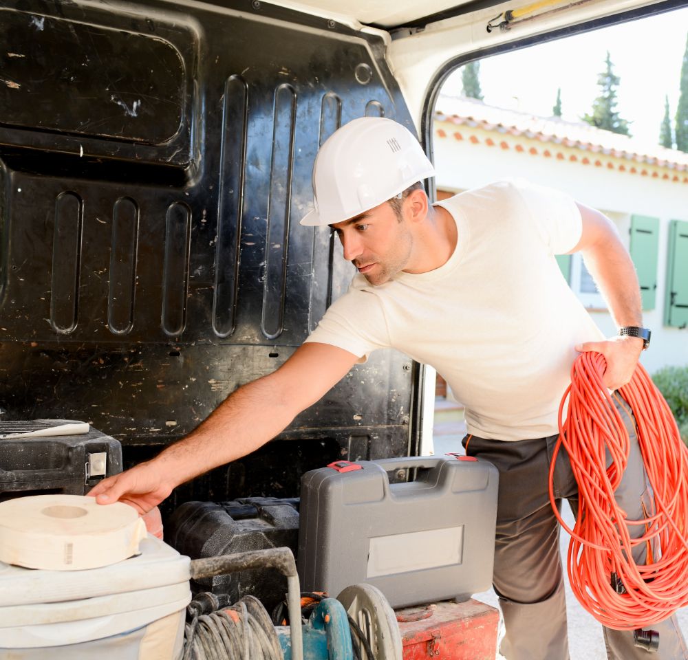Building wearing a hard hat reaching in van to get tools