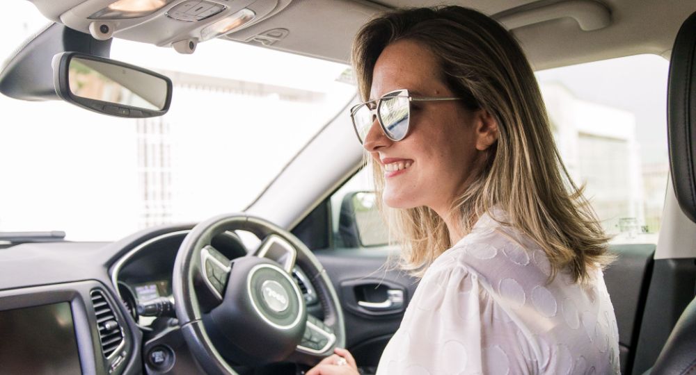 Woman with sunglasses in the driving seat smiling while looking outside