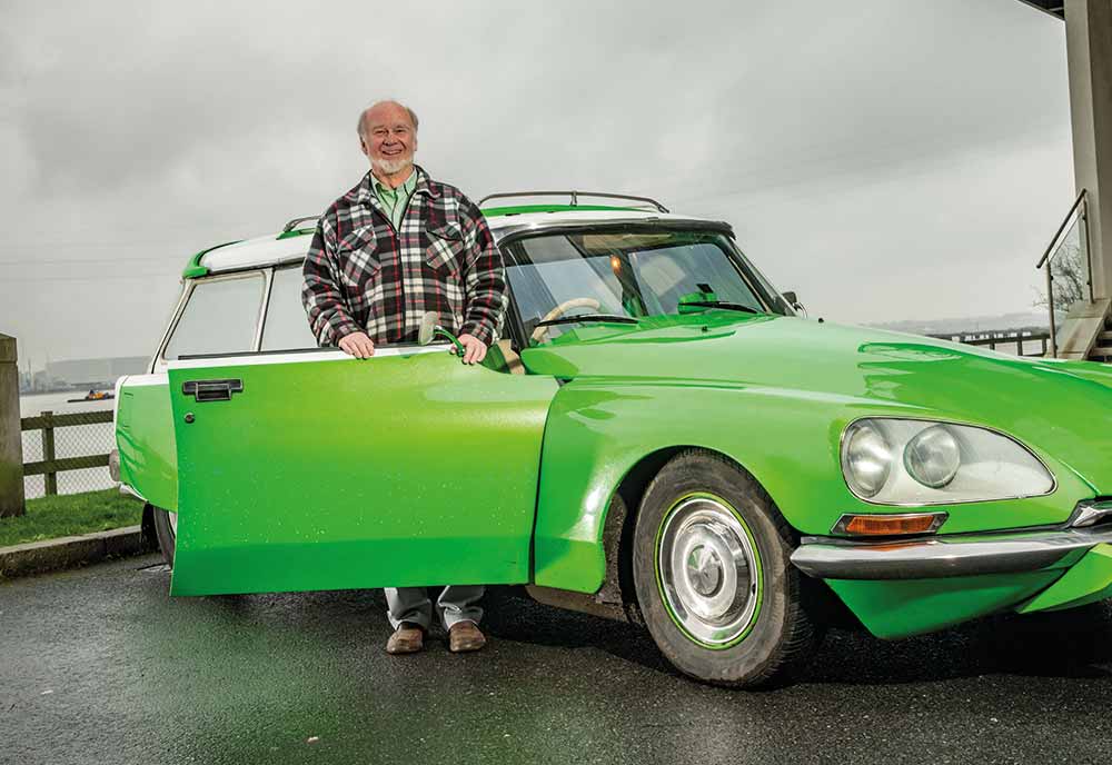Man standing next to his green Citroen DS with clouds in the background