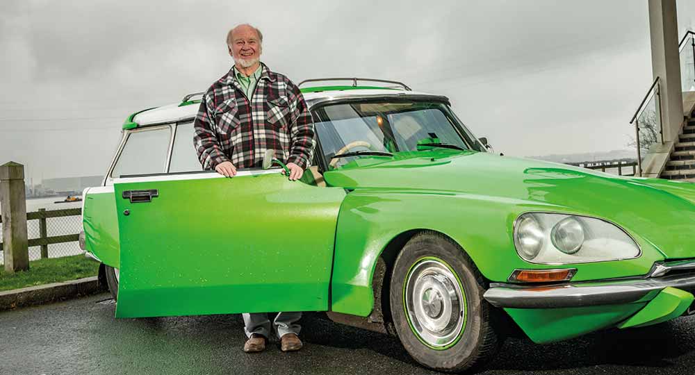 Man standing next to his green Citroen DS with clouds in the background