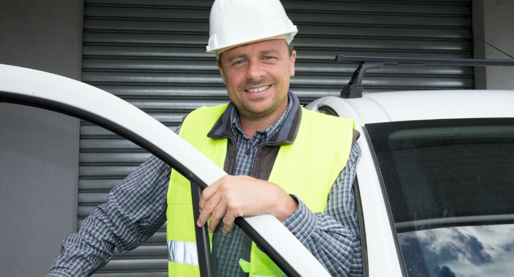 Man with hard hat and hi-vis vest on standing next to a van