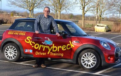 Driving instructor with his car in a car park