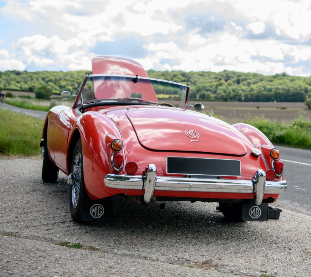 Red classic MG with its bonnet open pulled over on the side of a country road