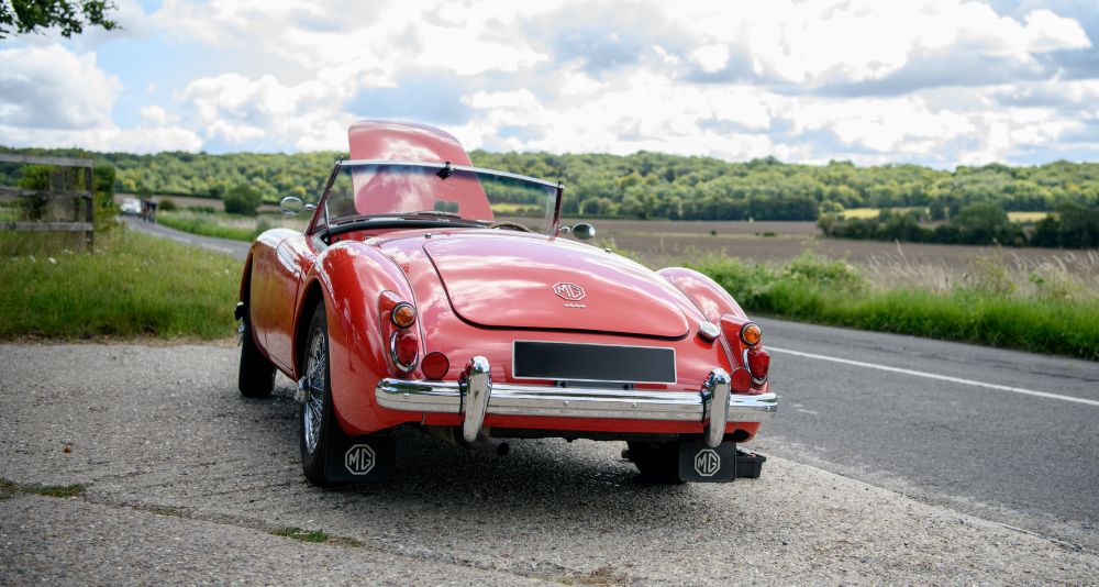 Red classic MG with its bonnet open pulled over on the side of a country road