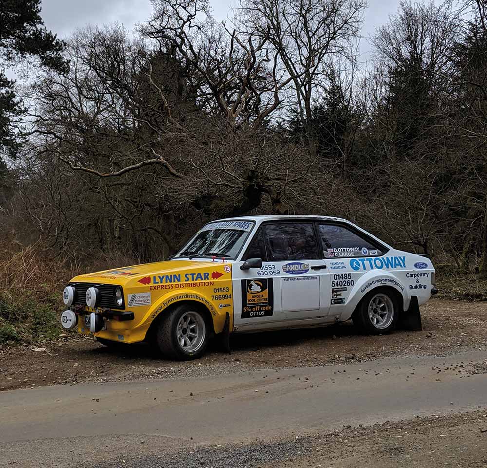 Yellow and white Ford Escort car parked in front of trees