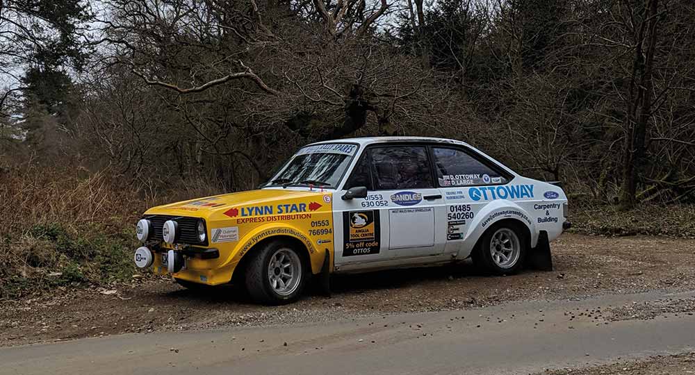 Yellow and white Ford Escort car parked in front of trees