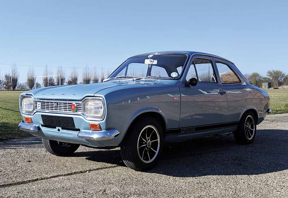 Silver Ford Escort parked on a gravel pathway in front of green grass and blue sky