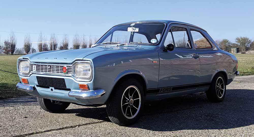 Silver Ford Escort parked on a gravel pathway in front of green grass and blue sky