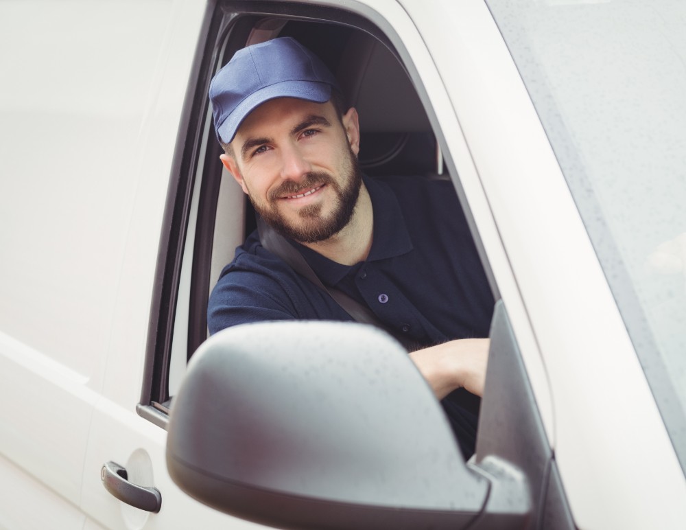 Tradesman in a blue hat, leaning out of a van window, smiling