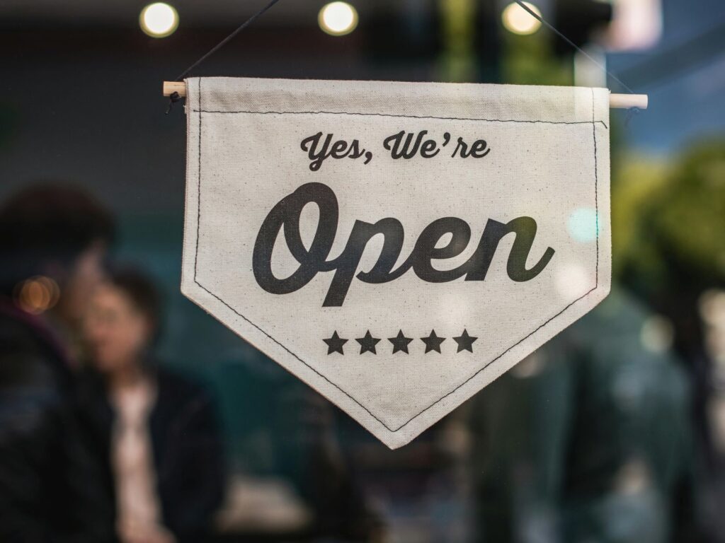 Close-up of 'Yes, we're open' with 5 stars sign hanging in shop window