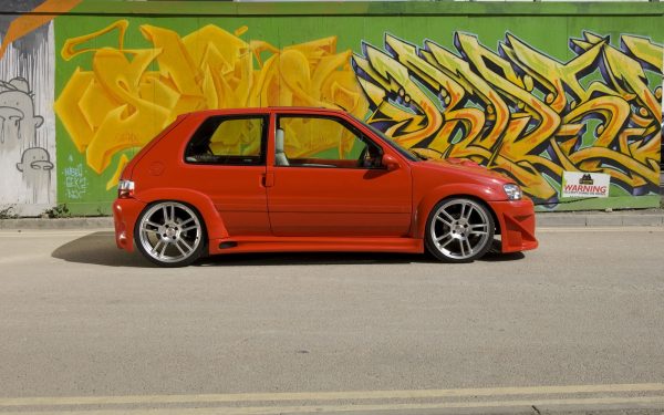 A modified car parked in front of graffiti on a wall.