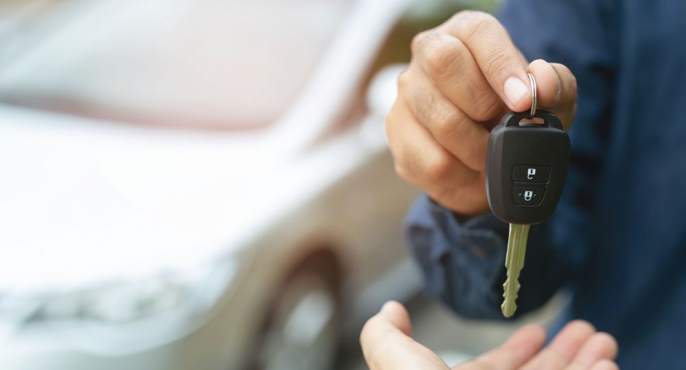 Car key being handed over with vehicle in the background