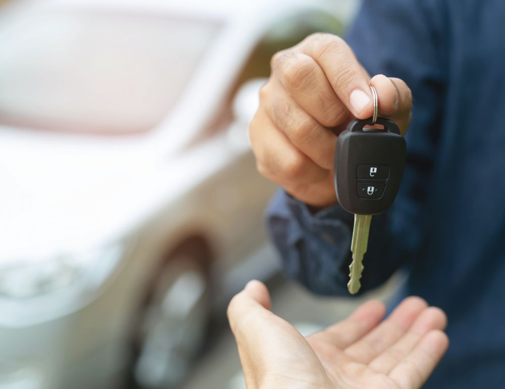 Car key being handed over with vehicle in the background