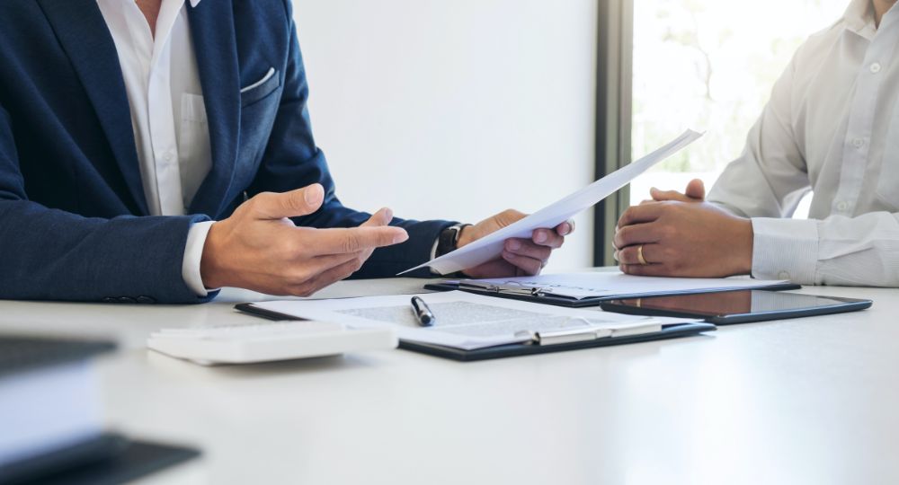 Two people in suits with paperwork on the desk