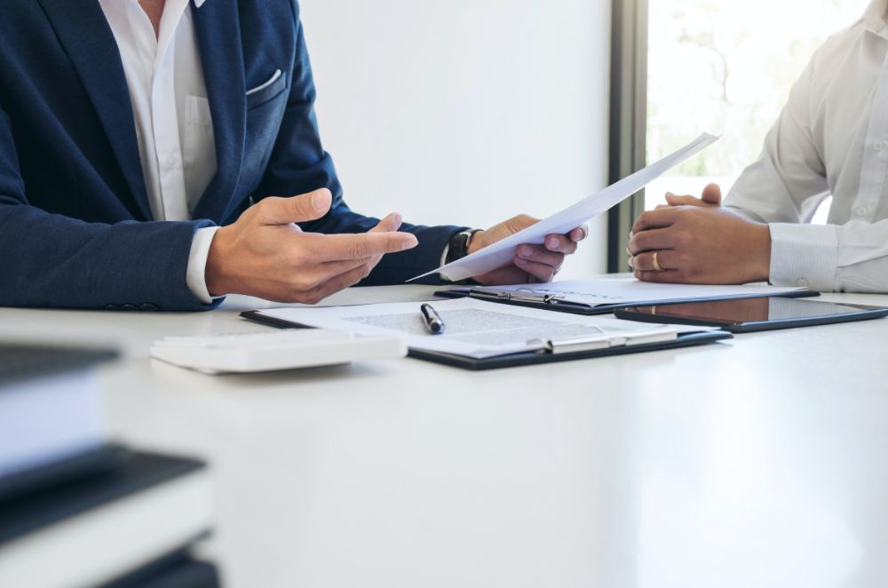 Two people in suits with paperwork on the desk