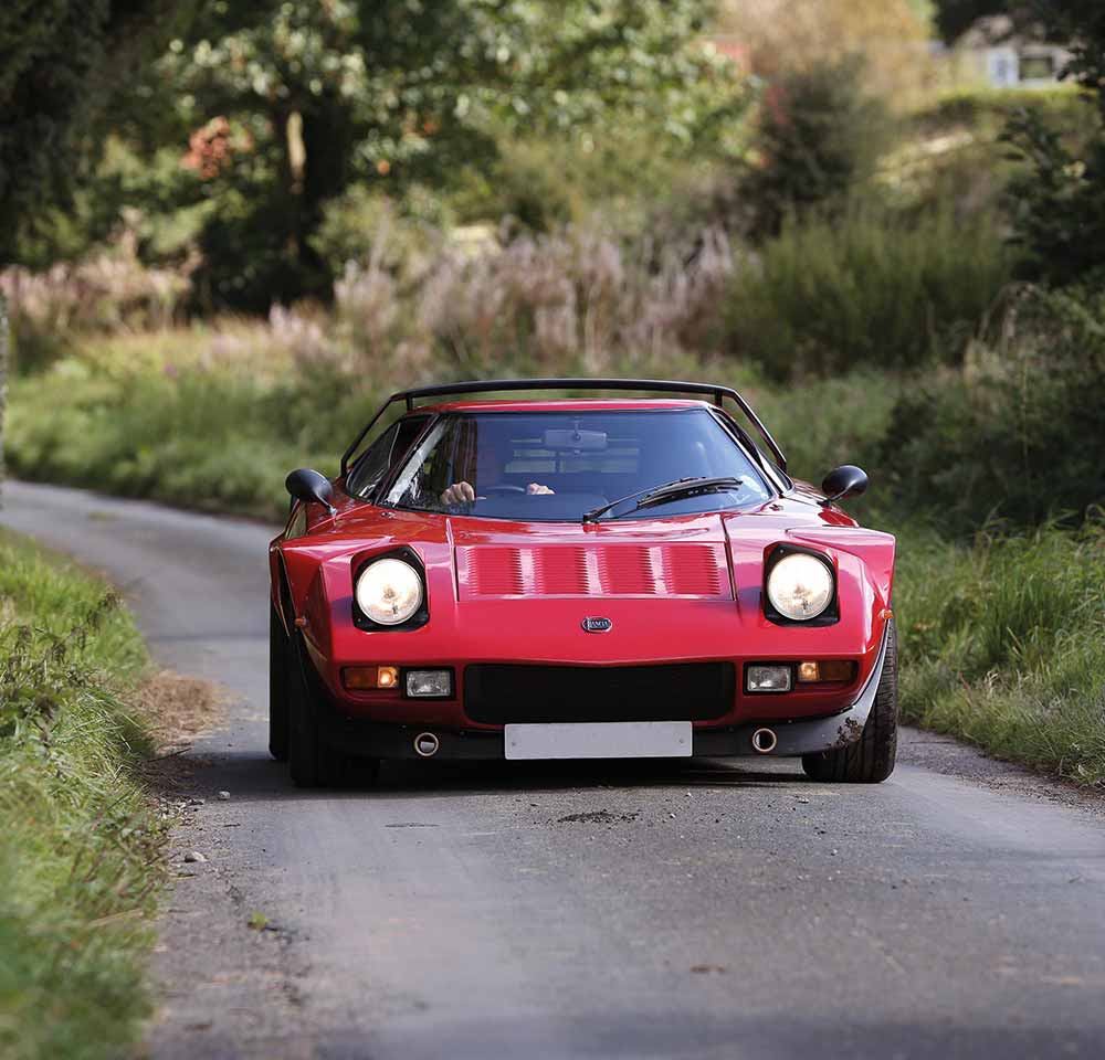 Red Lancia car driving down narrow road