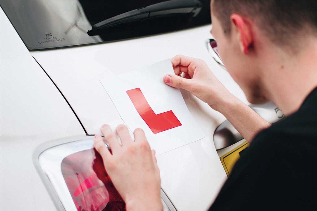 Young person sticking learner driver sign to the back of his car