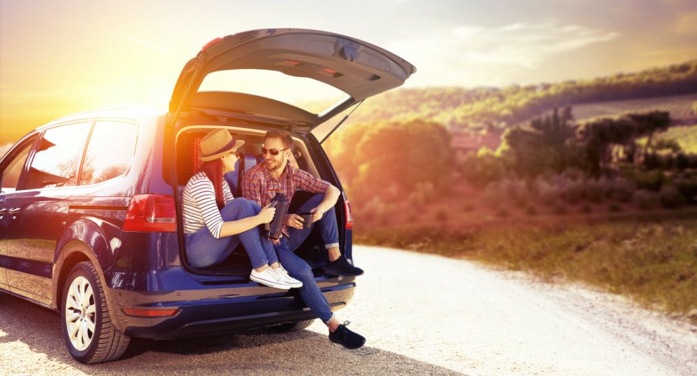 Two people sitting in the back of a car with sun setting in background