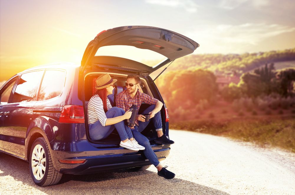 Two people sitting in the back of a car with sun setting in background