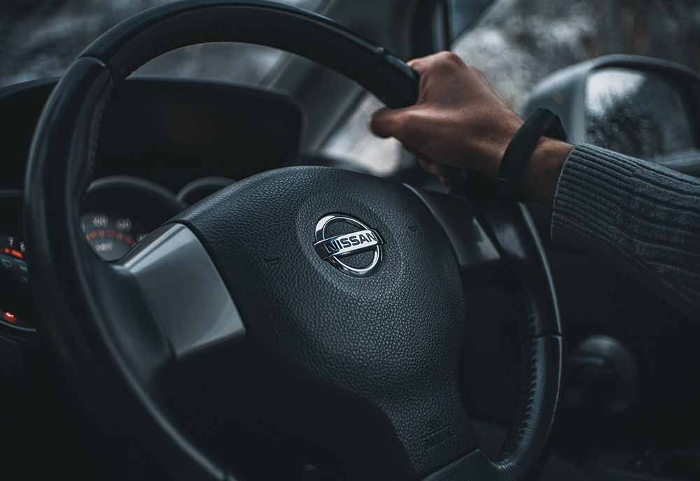Person's hand on a Nissan steering wheel