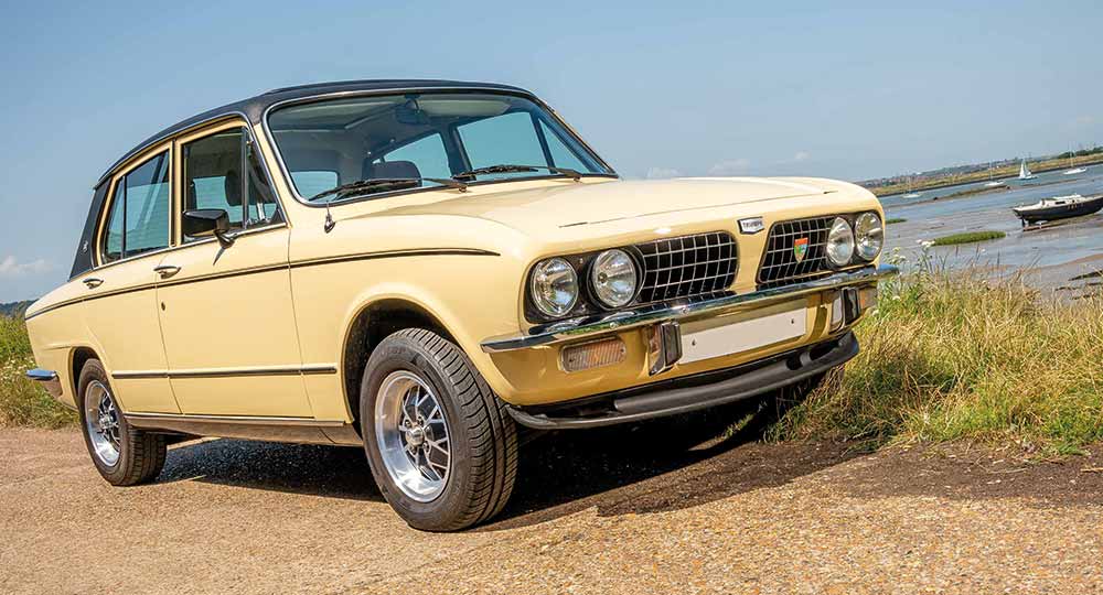 Yellow Triumph car pictured near water with sky in background