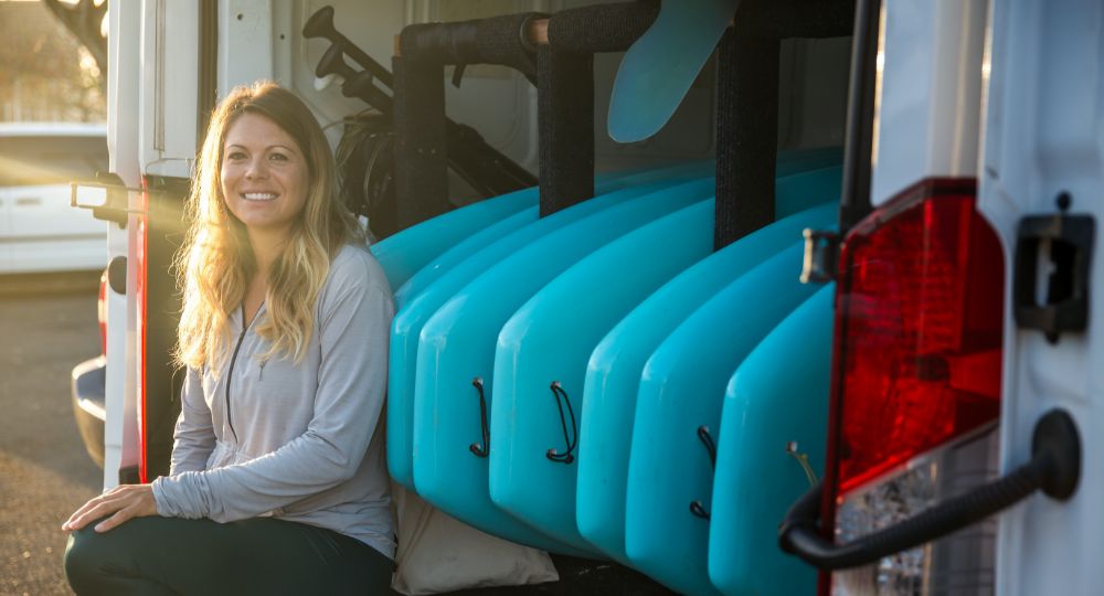 Woman in front of open van with surf boards mounted in the back