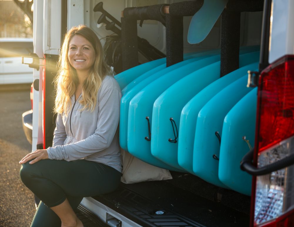 Woman in front of open van with surf boards mounted in the back